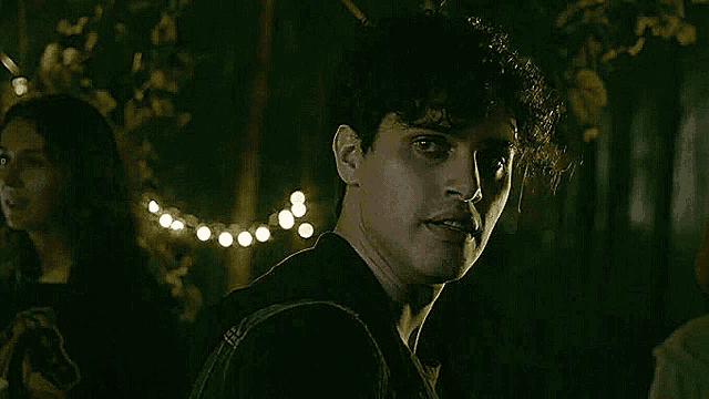 a young man with a backpack is standing in a dark room with a string of lights behind him .