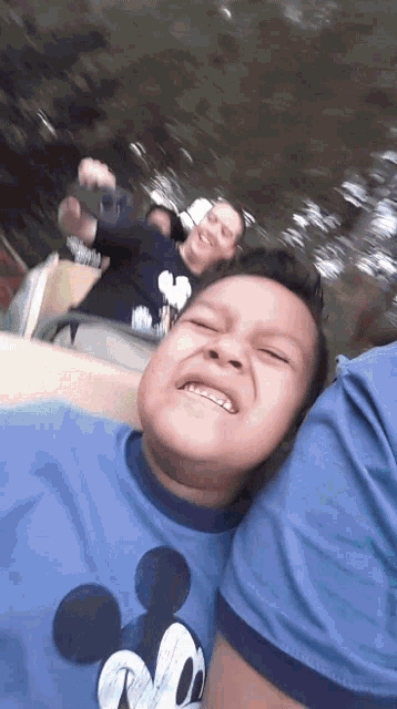 a young boy wearing a blue mickey mouse shirt is smiling