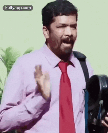 a man in a purple shirt and red tie is holding a camera and talking .