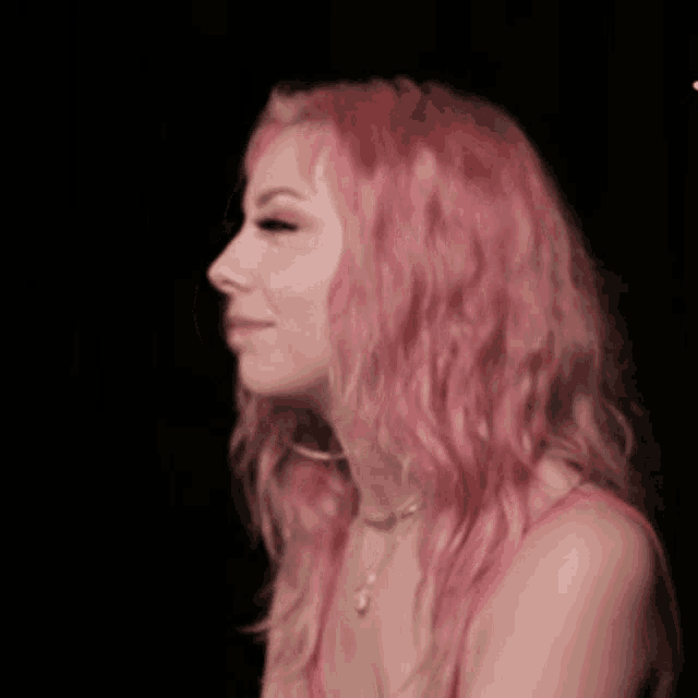a woman with pink hair is wearing a red tank top and a necklace .