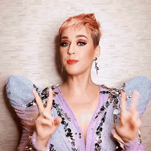 a woman with pink hair is wearing a purple dress and making a peace sign