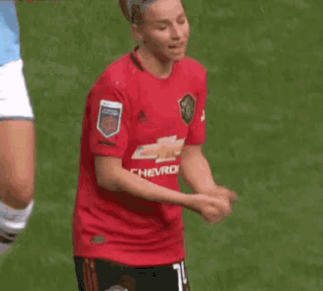 a woman in a red shirt is standing on a soccer field with her hands outstretched .