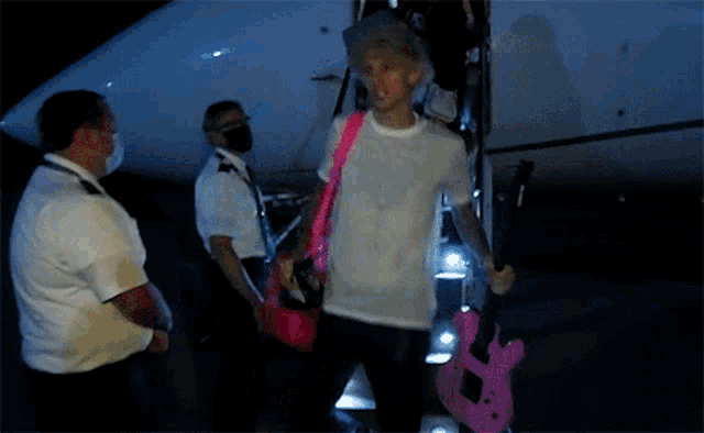 a man in a white shirt is holding a pink guitar and a pink purse