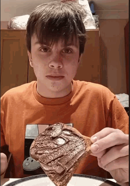 a young man wearing an orange shirt is holding a piece of food