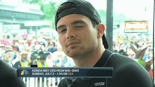 a man wearing a baseball cap stands in front of a sign that says honda indy 200 from mid-ohio sunday july 2