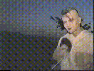 a man with a shaved head is standing in a field with a blue sky in the background