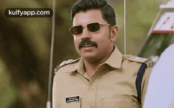 a police officer wearing sunglasses and a mustache is standing in front of a car .