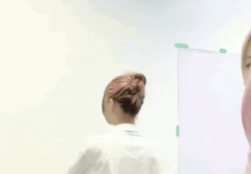 a woman with blonde hair is standing in front of a white wall with a bun on her head .