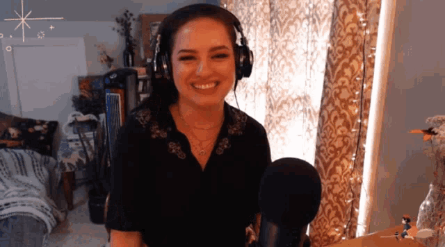 a woman wearing headphones stands in front of a microphone and smiles