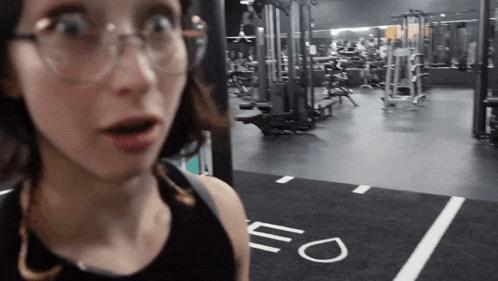 a woman wearing glasses is standing in a gym with the letter o on the floor