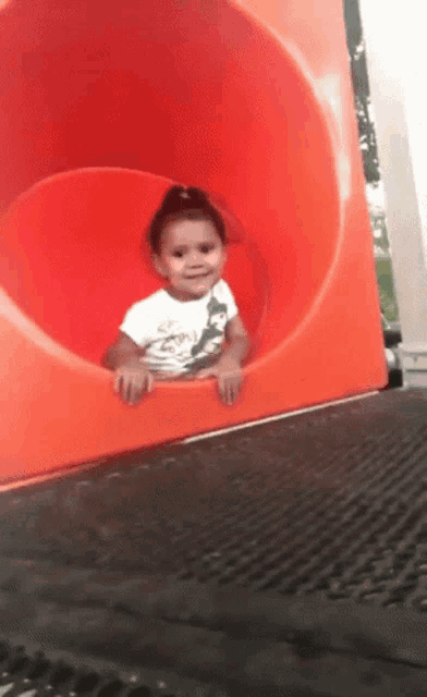 a little girl in a white shirt is going down a red slide