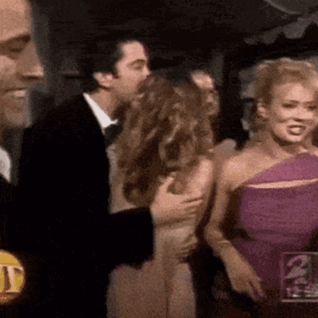 a man in a tuxedo is kissing a woman in a purple dress at a party .