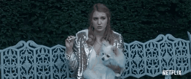 a woman in a sequined jacket is holding a small white dog while smoking a cigarette .