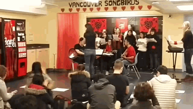 a group of people sitting in front of a vancouver songbirds sign