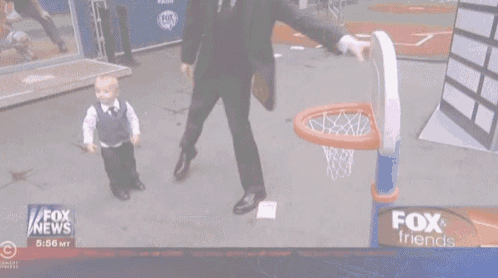 a man in a suit is playing basketball with a little boy in front of a fox news sign