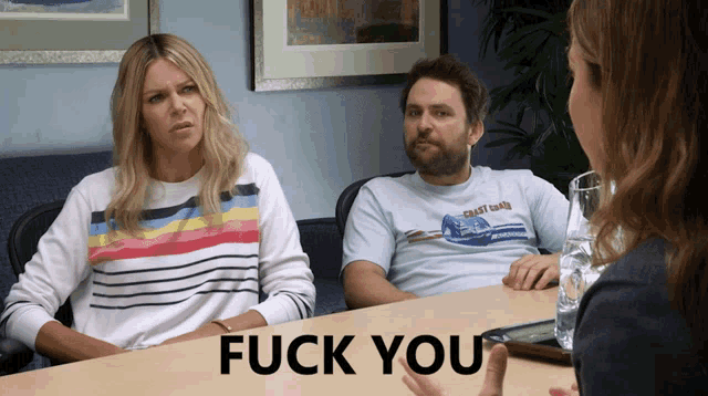 a man and a woman sit at a table with the words fuck you written on the table