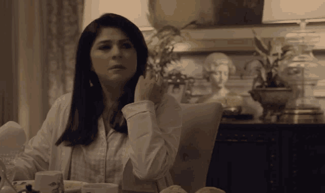 a woman in a white shirt sits at a table with a statue in the background