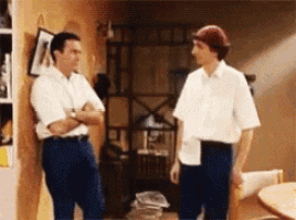 two men standing next to each other talking in a living room
