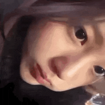a close up of a woman 's face with her mouth open and a glass of water in her hand .