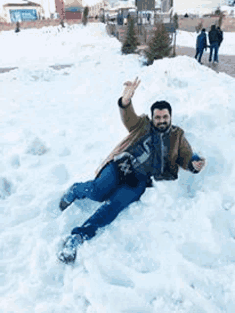 a man is laying on top of a pile of snow and making a peace sign .