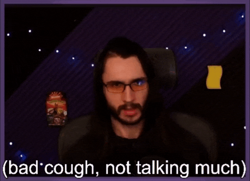 a man with long hair and glasses is sitting in front of a screen that says " bad cough not talking much "