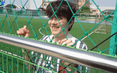 a young man behind a fence with a soccer field behind him
