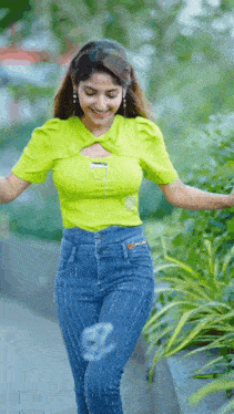 a woman in a lime green top and blue jeans is standing in front of a bush