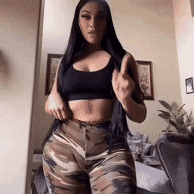 a woman in a black top and camouflage pants is standing in front of a mirror .