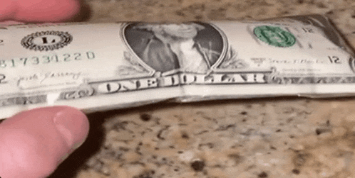 a person is holding a dollar bill in their hand on a counter .