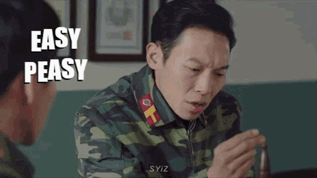 a man in a camouflage uniform is sitting at a table talking to another man and says easy peasy