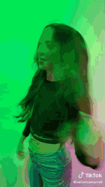 a woman in a crop top is dancing in front of a green background with tiktok written on the bottom
