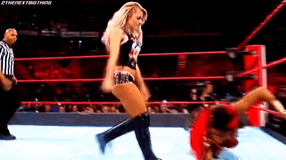 a woman is standing on top of another woman in a wrestling ring while a referee watches .