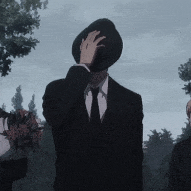 a man in a suit and tie covers his face with his hat