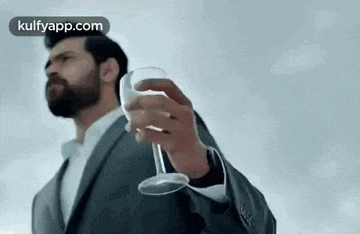 a man in a suit is holding a glass of wine in his right hand .