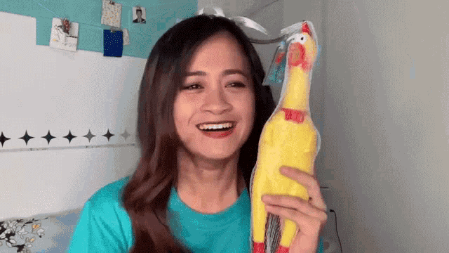 a woman in a blue shirt is holding a stuffed chicken and smiling