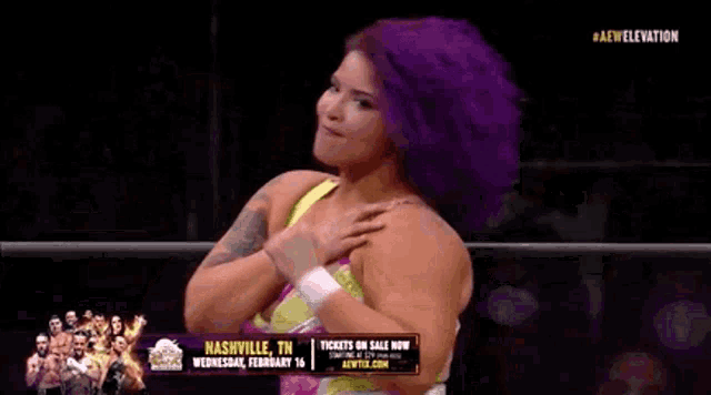 a female wrestler with purple hair is standing in a ring with her hands on her chest .