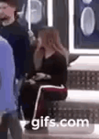 a woman is sitting on a bench talking on a cell phone in a crowd of people .