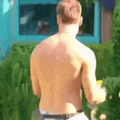 a shirtless man is standing in front of a window and holding a bottle of water .