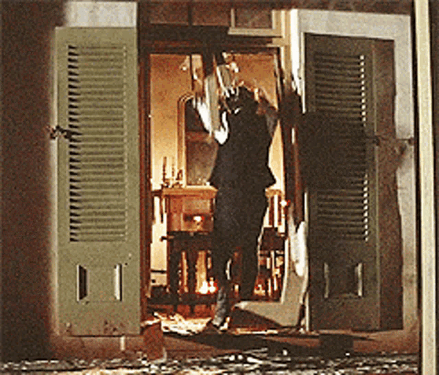 a man in a suit stands in a room with shutters open