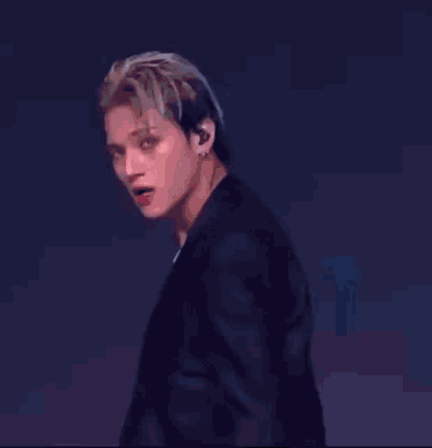 a man in a black suit and a necklace is dancing on a stage .