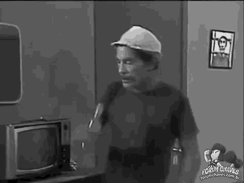 a man wearing a hat is standing in front of a television .