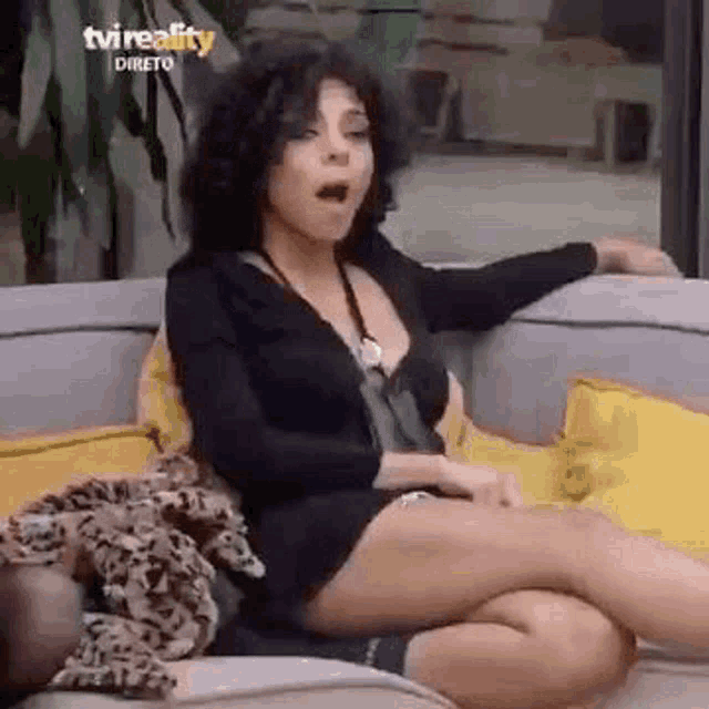 a woman is sitting on a couch with her legs crossed and making a funny face .