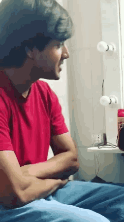 a man in a red shirt sits with his arms crossed in front of a mirror