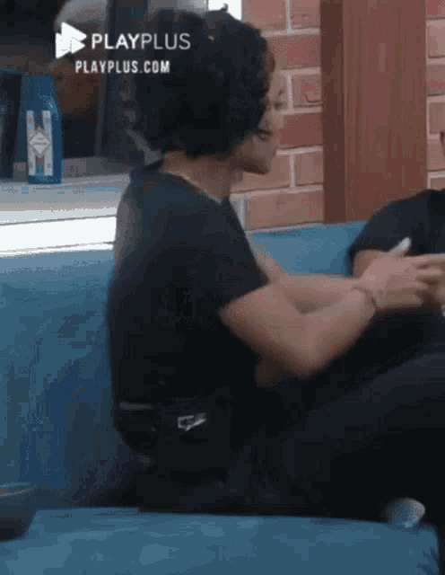 a woman in a black shirt is sitting on a blue couch talking to a man .