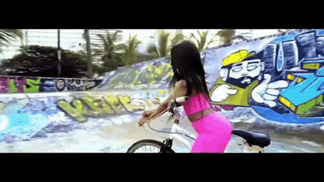 a woman riding a bike in front of a graffiti wall
