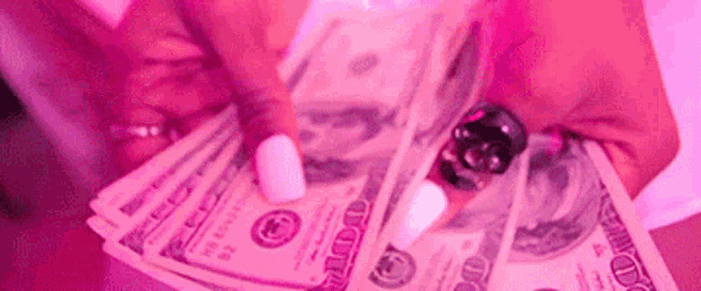 a woman is holding a bunch of money in her hands in a pink light .