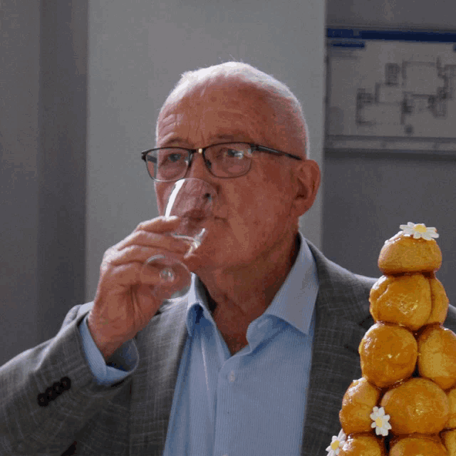 a man in a suit is drinking from a glass in front of a stack of pastries