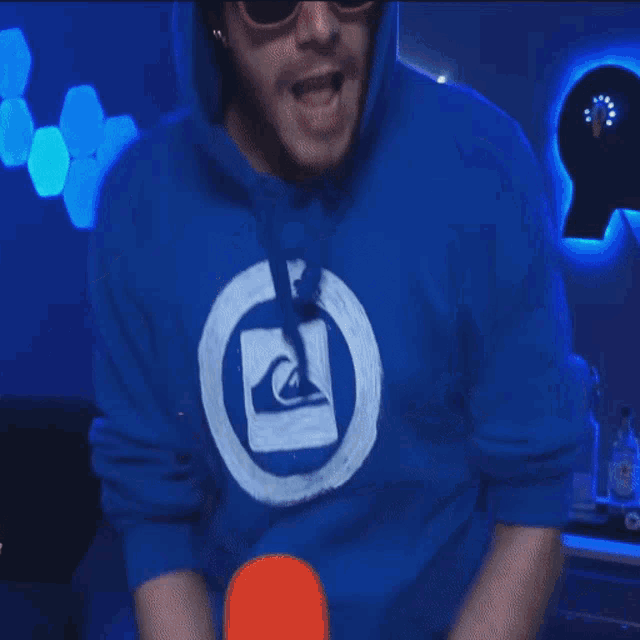 a man wearing a blue quiksilver hoodie and sunglasses is dancing in front of a microphone .