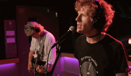 a man singing into a microphone while another man plays guitar