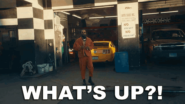 a man in an orange suit is standing in front of a garage with the words what 's up